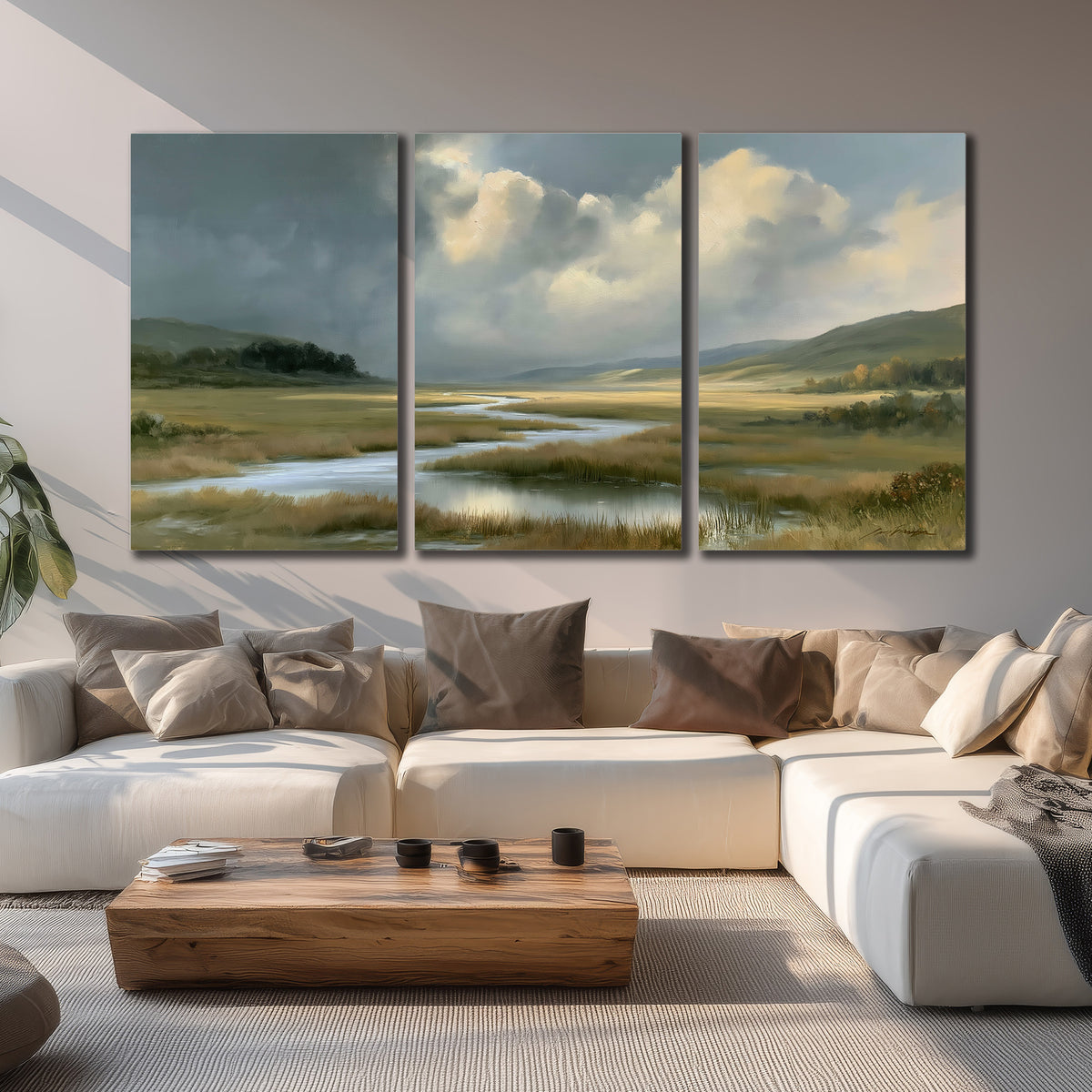 A winding stream through an open meadow beneath large sunlit clouds 3 piece canvas wall art displayed in a living room