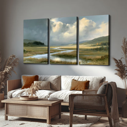 A winding stream through an open meadow beneath large sunlit clouds 3 piece canvas wall art displayed in a rustic living room