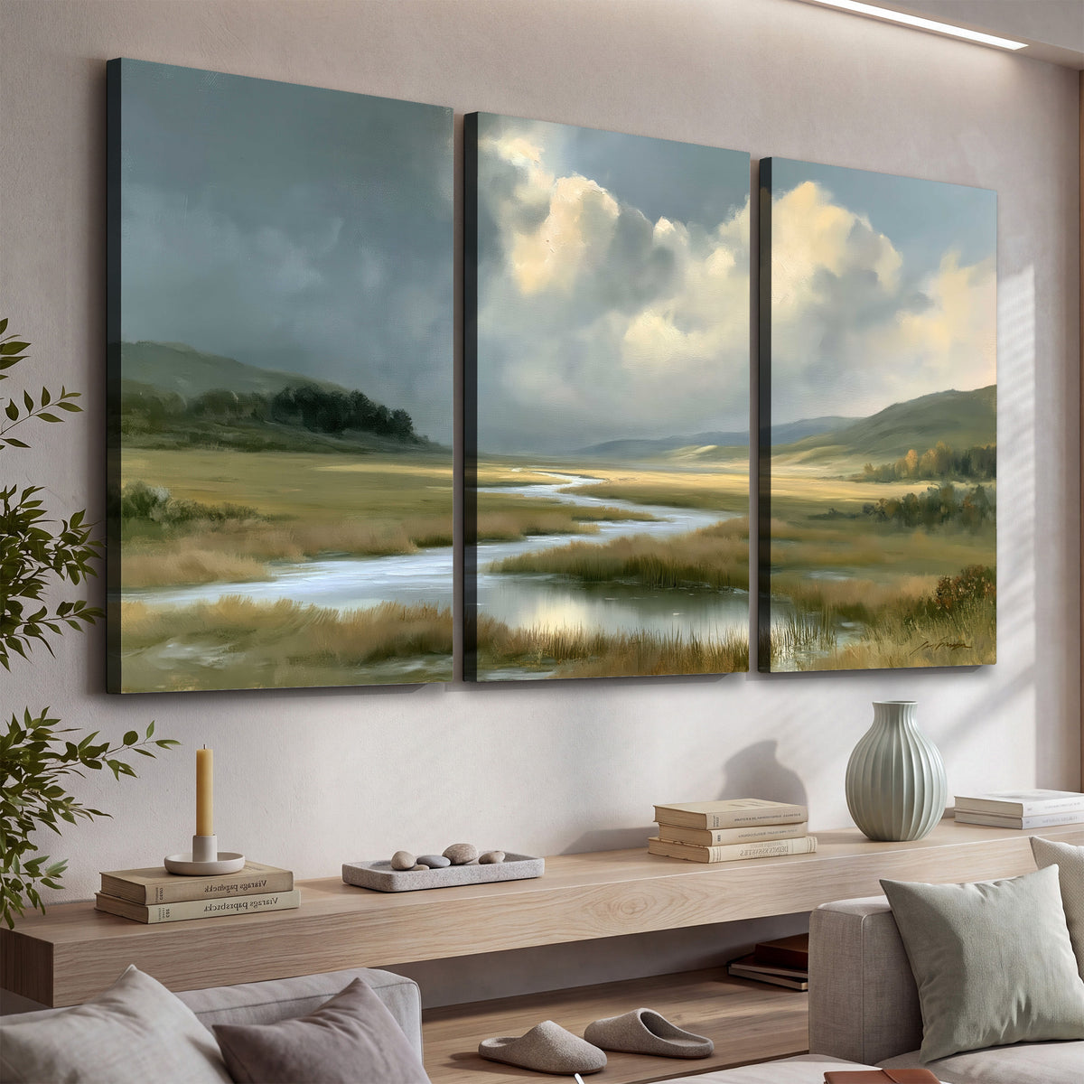 A winding stream through an open meadow beneath large sunlit clouds 3 piece canvas wall art displayed in a console