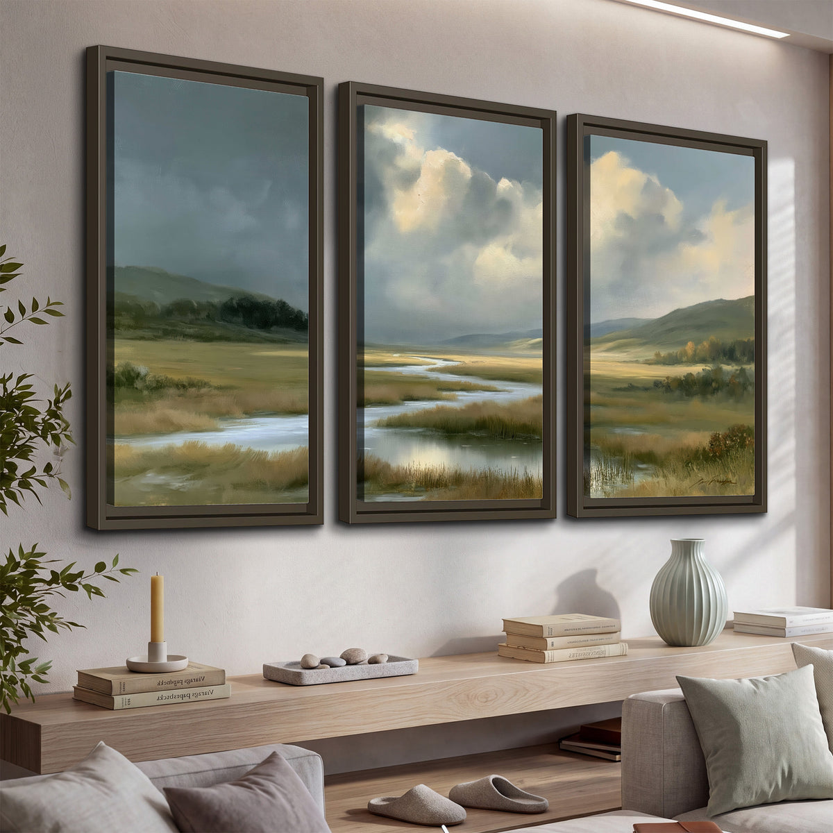 A winding stream through an open meadow beneath large sunlit clouds 3 piece framed canvas wall art displayed in a console