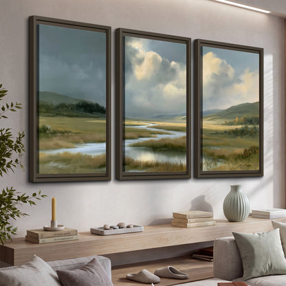 A winding stream through an open meadow beneath large sunlit clouds 3 piece framed canvas wall art displayed in a console
