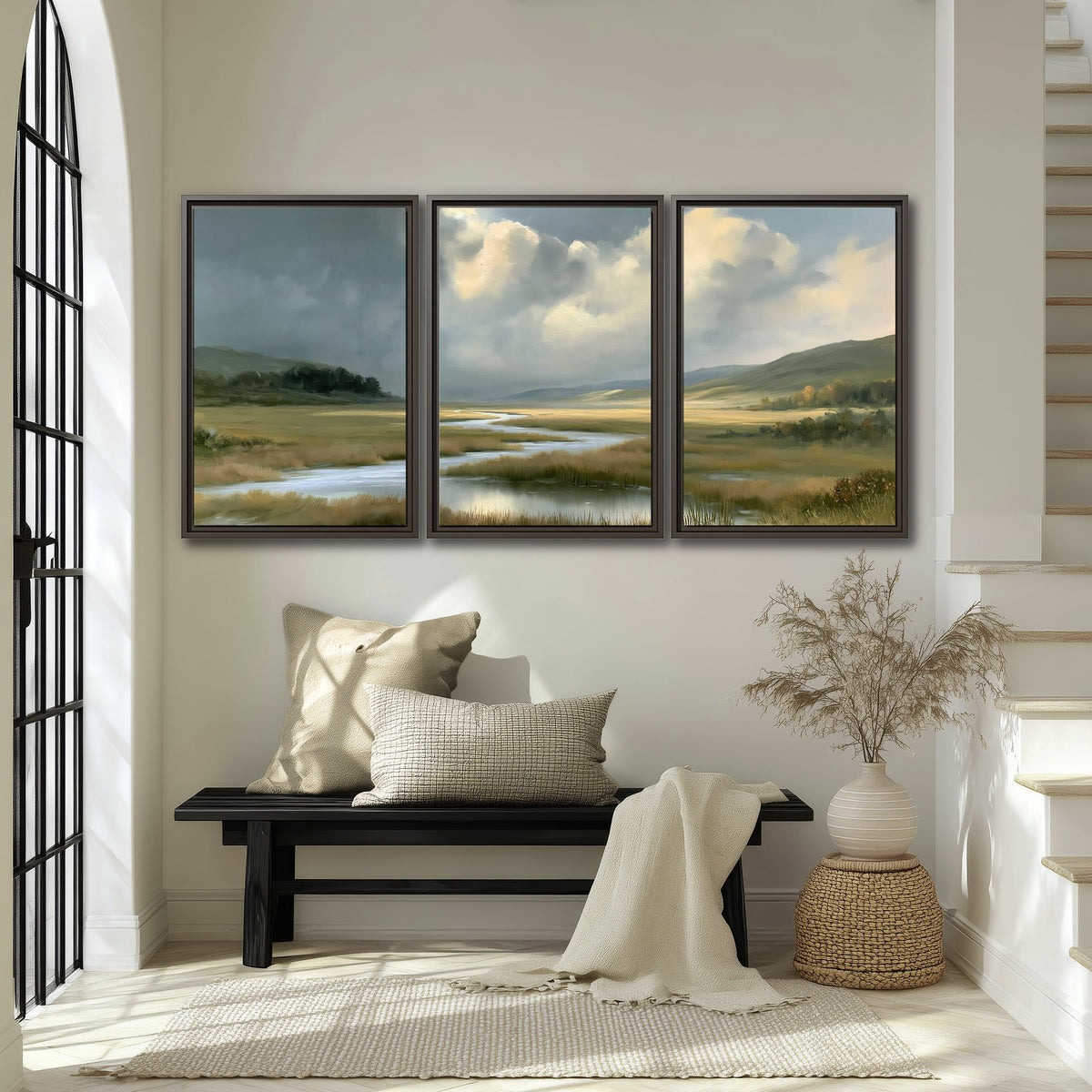 A winding stream through an open meadow beneath large sunlit clouds 3 piece framed canvas wall art displayed in a entryway