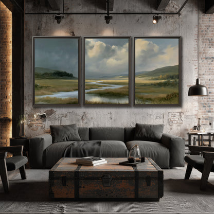 A winding stream through an open meadow beneath large sunlit clouds 3 piece framed canvas wall art displayed in a industrial room