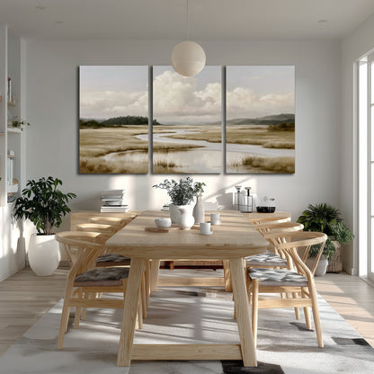 A pale winding waterway crossing quiet wetlands beneath billowing white clouds 3 piece canvas wall art room and product view