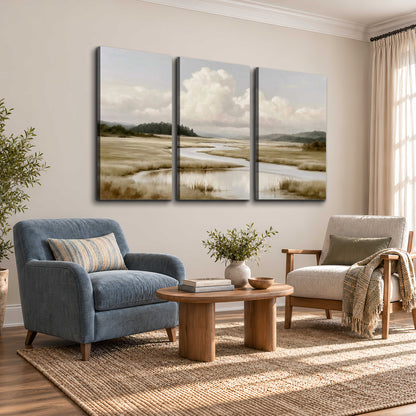 A pale winding waterway crossing quiet wetlands beneath billowing white clouds 3 piece canvas wall art styled in an interior