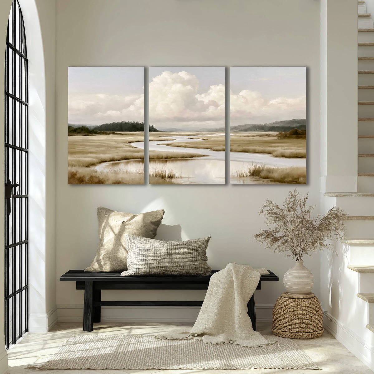 A pale winding waterway crossing quiet wetlands beneath billowing white clouds 3 piece canvas wall art displayed in a entryway