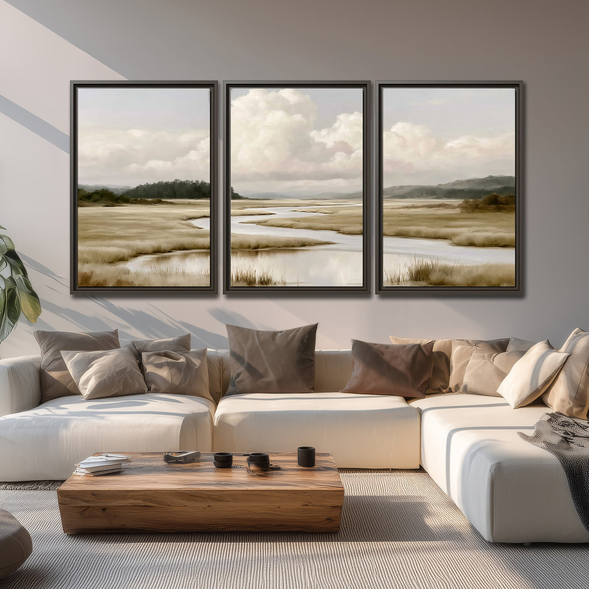 A pale winding waterway crossing quiet wetlands beneath billowing white clouds 3 piece framed canvas wall art displayed in a living room