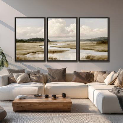 A pale winding waterway crossing quiet wetlands beneath billowing white clouds 3 piece framed canvas wall art displayed in a living room