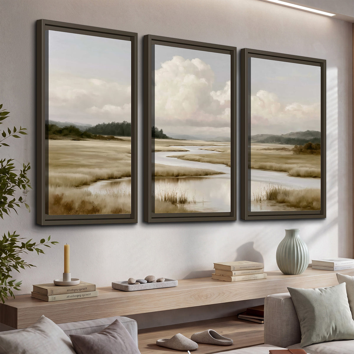 A pale winding waterway crossing quiet wetlands beneath billowing white clouds 3 piece framed canvas wall art displayed in a console