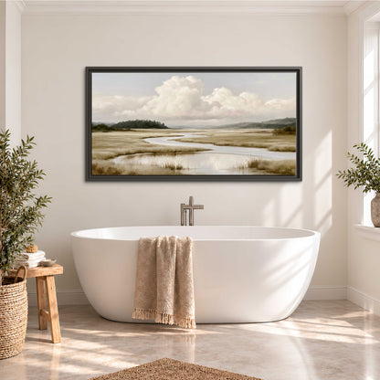 A pale winding waterway crossing quiet wetlands beneath billowing white clouds single framed canvas wall art styled in an interior