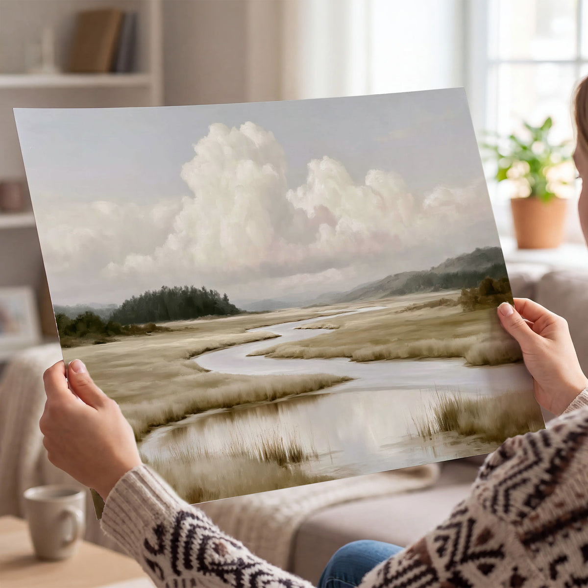 A pale winding waterway crossing quiet wetlands beneath billowing white clouds single poster print held in hands
