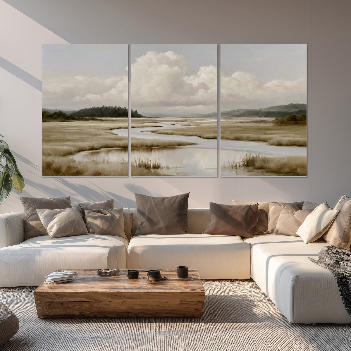 A pale winding waterway crossing quiet wetlands beneath billowing white clouds set of 3 poster prints displayed in a living room