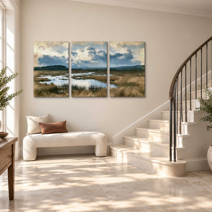 A wide open marsh with blue water and warm grasses beneath layered clouds 3 piece canvas wall art styled in an interior