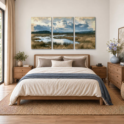 A wide open marsh with blue water and warm grasses beneath layered clouds 3 piece canvas wall art styled in an interior