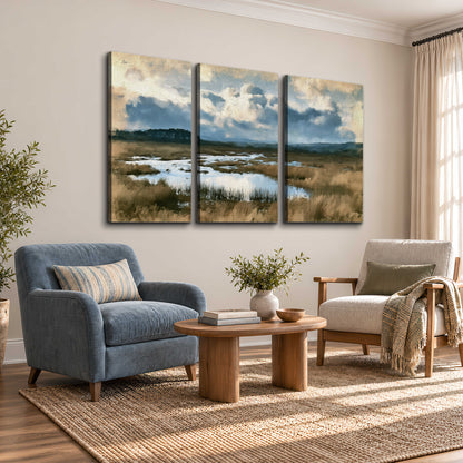 A wide open marsh with blue water and warm grasses beneath layered clouds 3 piece canvas wall art styled in an interior