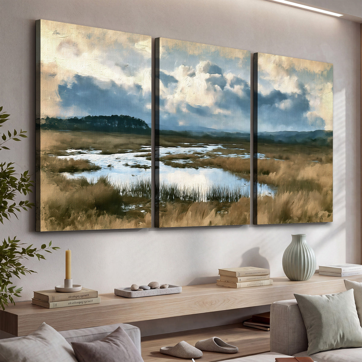 A wide open marsh with blue water and warm grasses beneath layered clouds 3 piece canvas wall art displayed in a console