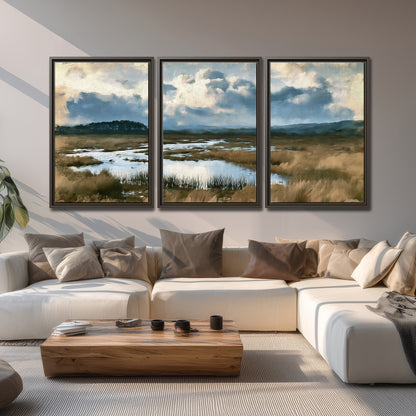 A wide open marsh with blue water and warm grasses beneath layered clouds 3 piece framed canvas wall art displayed in a living room