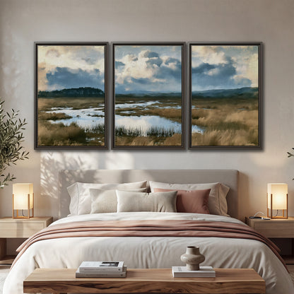 A wide open marsh with blue water and warm grasses beneath layered clouds 3 piece framed canvas wall art displayed in a bedroom