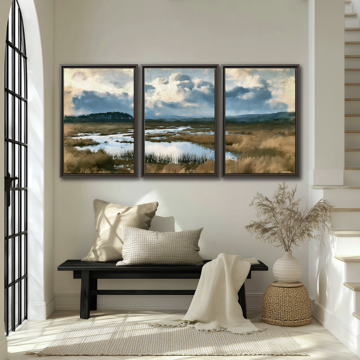 A wide open marsh with blue water and warm grasses beneath layered clouds 3 piece framed canvas wall art displayed in a entryway