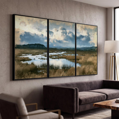 A wide open marsh with blue water and warm grasses beneath layered clouds 3 piece framed canvas wall art displayed in a modern living room