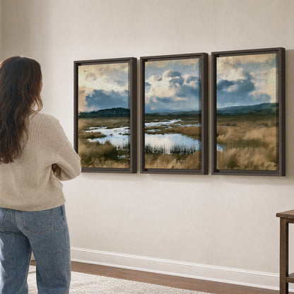 A wide open marsh with blue water and warm grasses beneath layered clouds 3 piece framed canvas wall art three panel arrangement on a wall
