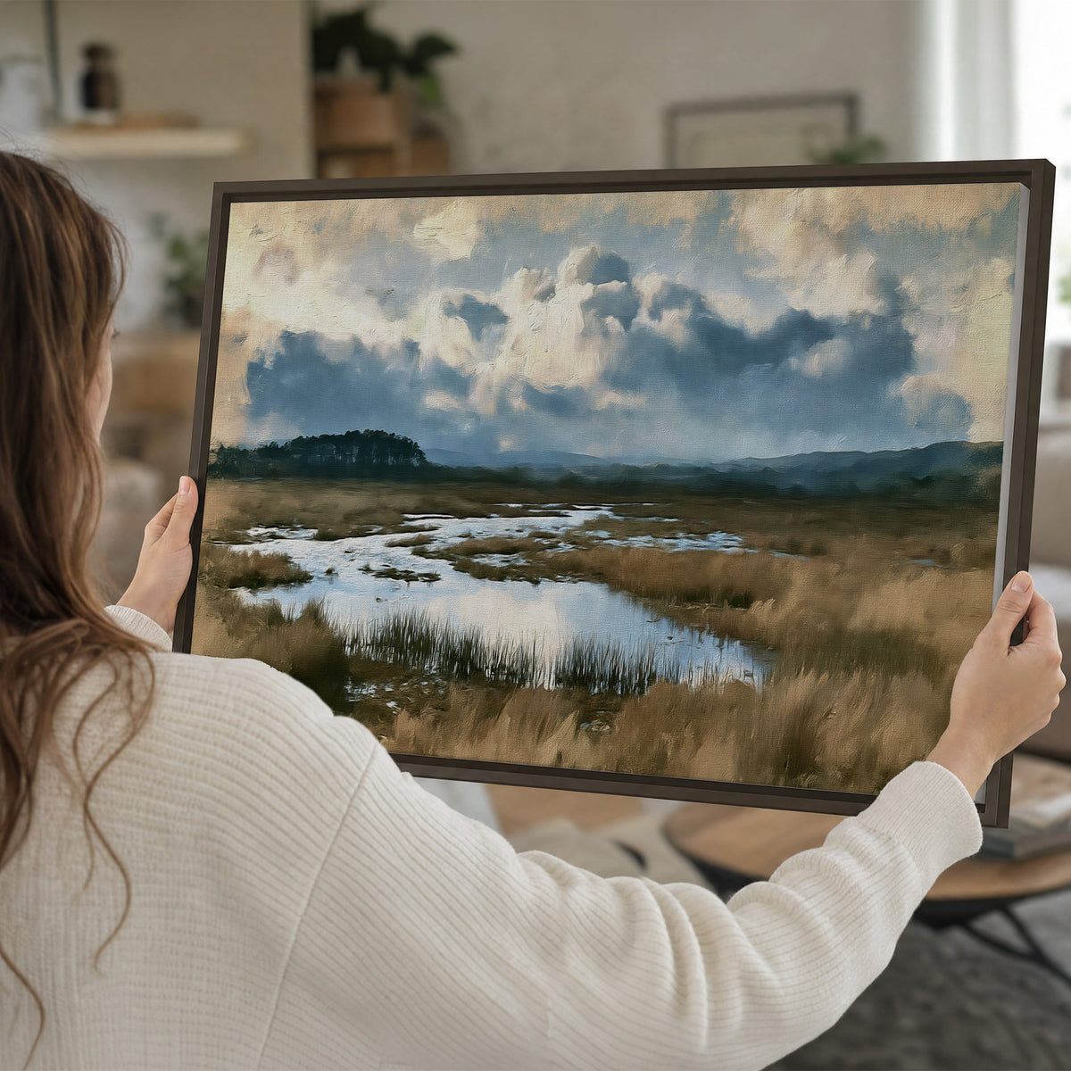 A wide open marsh with blue water and warm grasses beneath layered clouds single framed canvas wall art held in hands