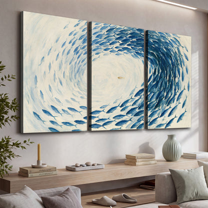 A circular school of blue fish flowing around a pale open center 3 piece canvas wall art displayed in a console