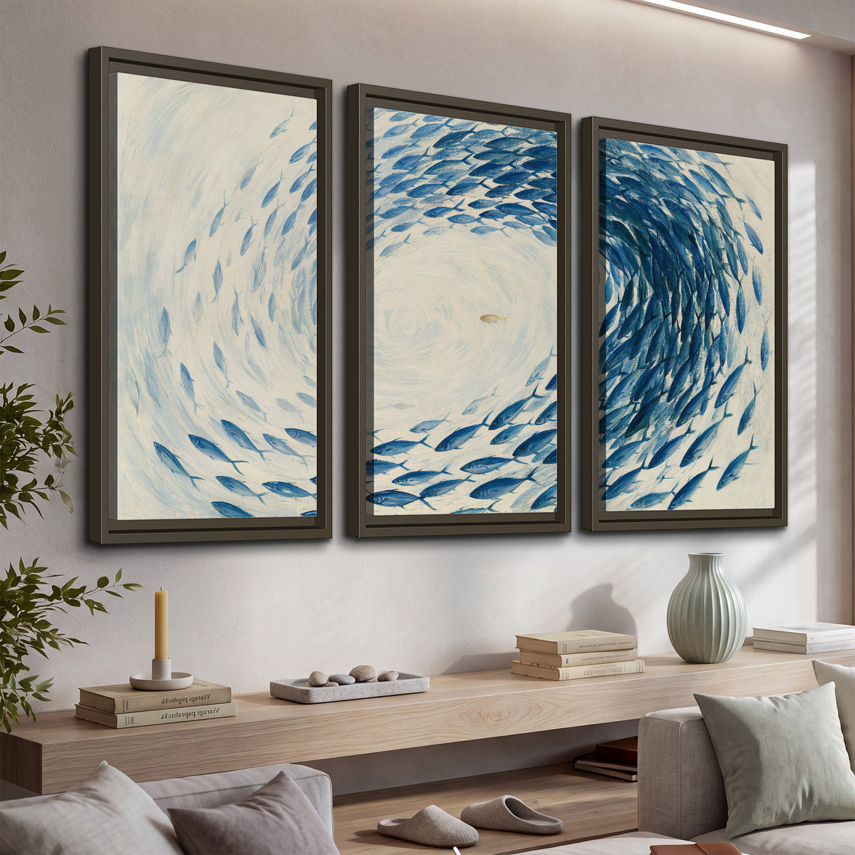 A circular school of blue fish flowing around a pale open center 3 piece framed canvas wall art displayed in a console