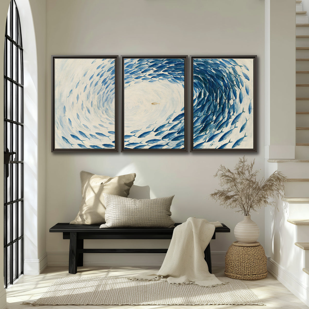 A circular school of blue fish flowing around a pale open center 3 piece framed canvas wall art displayed in a entryway