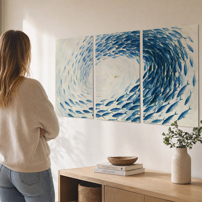 A circular school of blue fish flowing around a pale open center set of 3 poster prints three panel arrangement on a wall