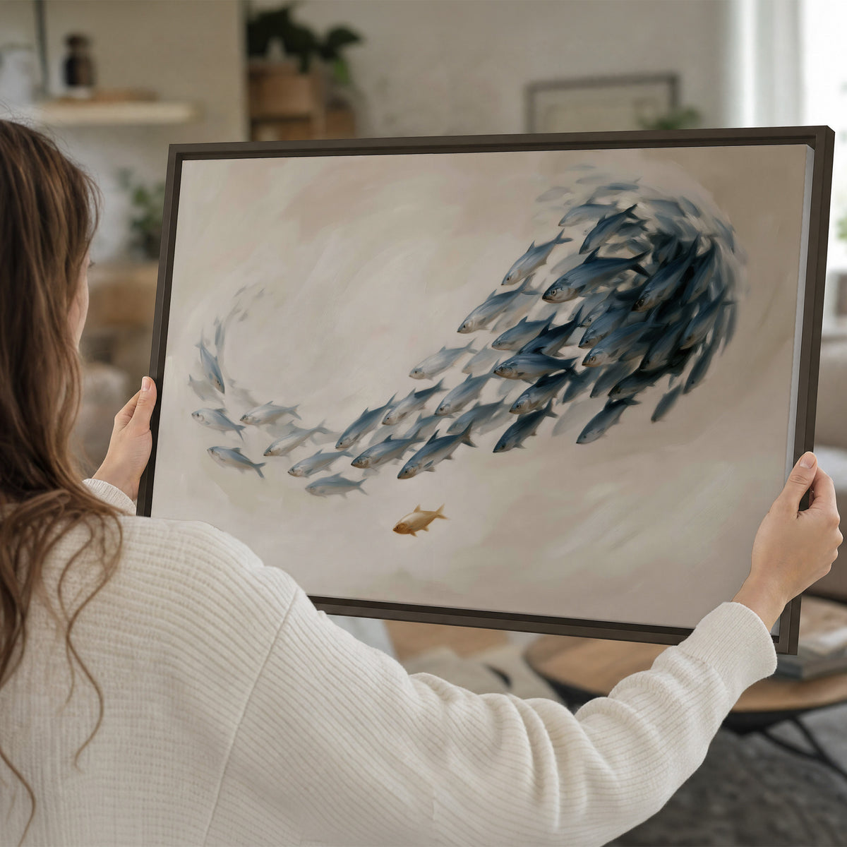 A sweeping school of small gray fish curving across a pale neutral background single framed canvas wall art held in hands