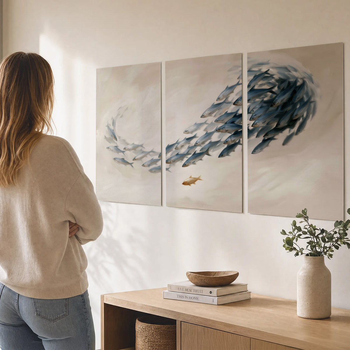 A sweeping school of small gray fish curving across a pale neutral background set of 3 poster prints three panel arrangement on a wall