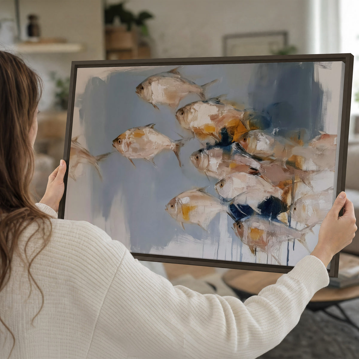 Small blue and golden fish moving across a pale layered abstract background single framed canvas wall art held in hands