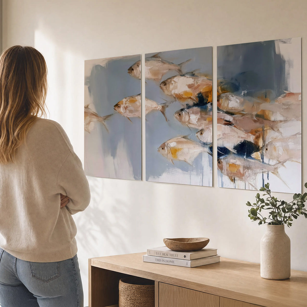 Small blue and golden fish moving across a pale layered abstract background set of 3 poster prints three panel arrangement on a wall