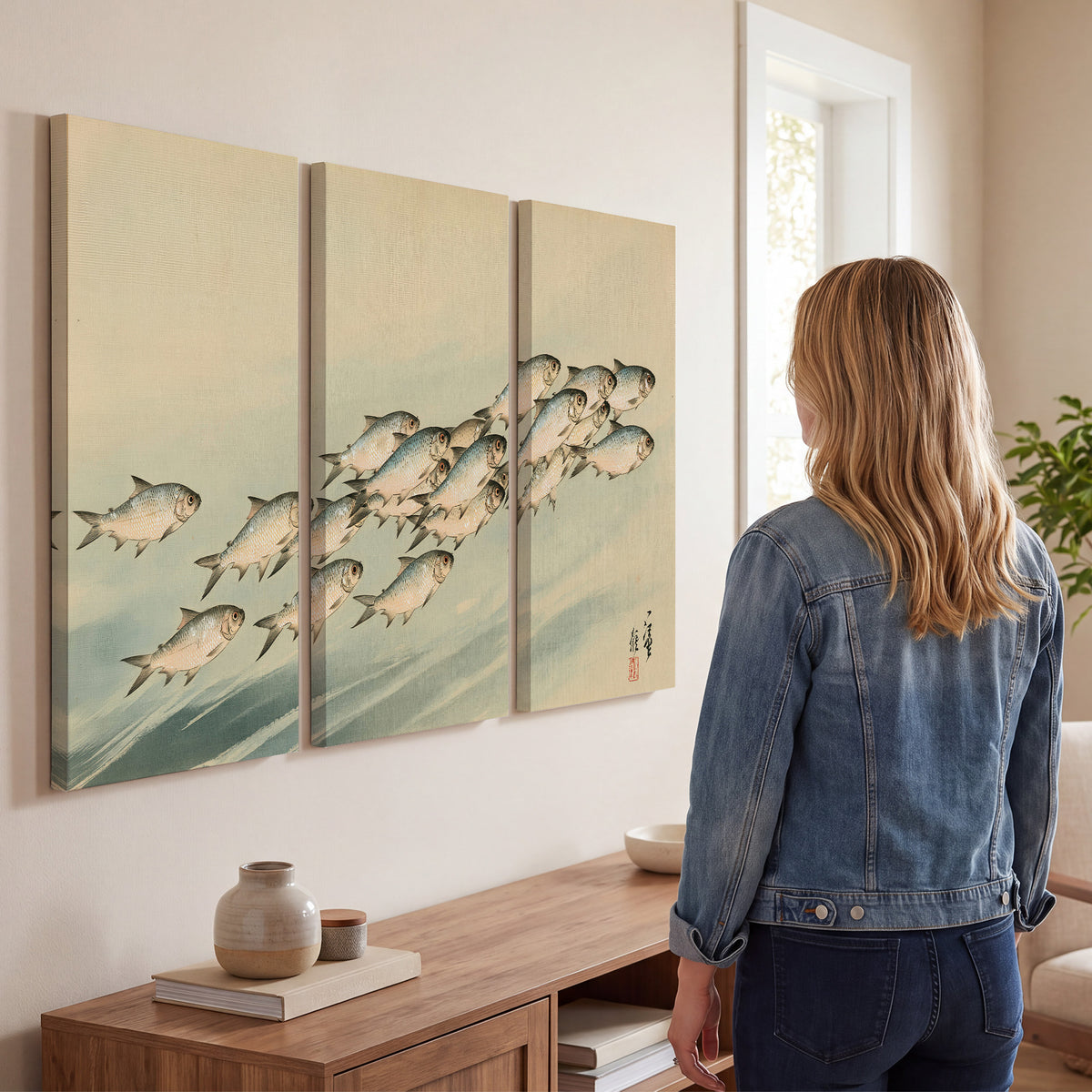 A flowing school of small fish above pale blue water on a cream ground 3 piece canvas wall art three panel arrangement on a wall