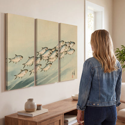 A flowing school of small fish above pale blue water on a cream ground 3 piece canvas wall art three panel arrangement on a wall