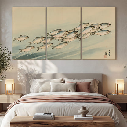 A flowing school of small fish above pale blue water on a cream ground 3 piece canvas wall art displayed in a bedroom