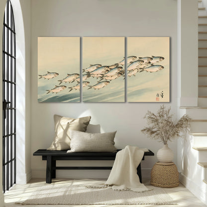 A flowing school of small fish above pale blue water on a cream ground 3 piece canvas wall art displayed in a entryway