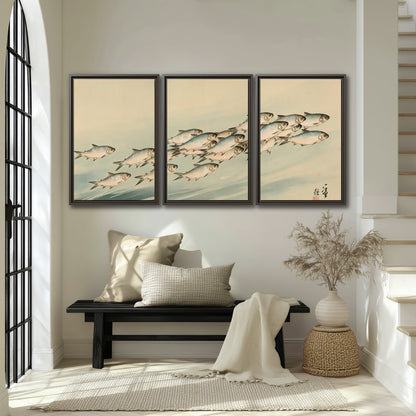A flowing school of small fish above pale blue water on a cream ground 3 piece framed canvas wall art displayed in a entryway