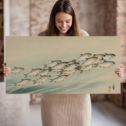 A flowing school of small fish above pale blue water on a cream ground single canvas wall art held in hands