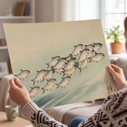 A flowing school of small fish above pale blue water on a cream ground single poster print held in hands