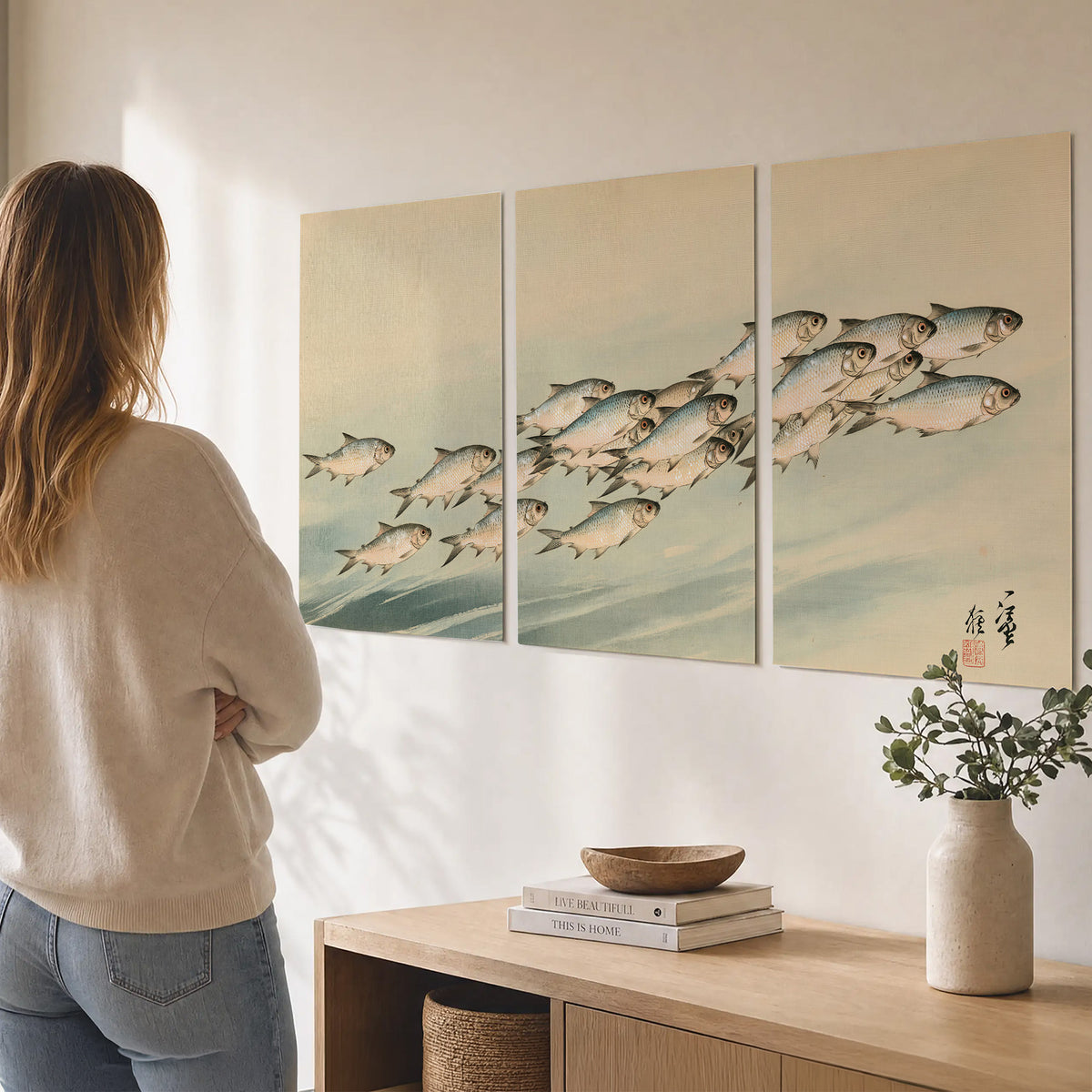A flowing school of small fish above pale blue water on a cream ground set of 3 poster prints three panel arrangement on a wall