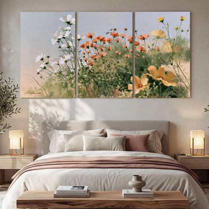 White and orange meadow flowers with fine green stems under a pale sky 3 piece canvas wall art displayed in a bedroom