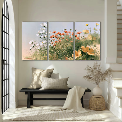 White and orange meadow flowers with fine green stems under a pale sky 3 piece canvas wall art displayed in a entryway