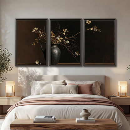 Fine flowering branches in a small dark vase on a wooden table against a deep brown background 3 piece framed canvas wall art displayed in a bedroom