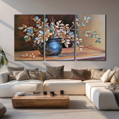 White and peach flowering branches arranged in a blue vase against a warm ochre background 3 piece canvas wall art displayed in a living room