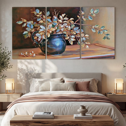 White and peach flowering branches arranged in a blue vase against a warm ochre background 3 piece canvas wall art displayed in a bedroom