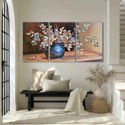 White and peach flowering branches arranged in a blue vase against a warm ochre background 3 piece canvas wall art displayed in a entryway