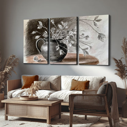 Fine leafy branches spilling from a dark rounded vase in a soft monochrome still life 3 piece canvas wall art displayed in a rustic living room