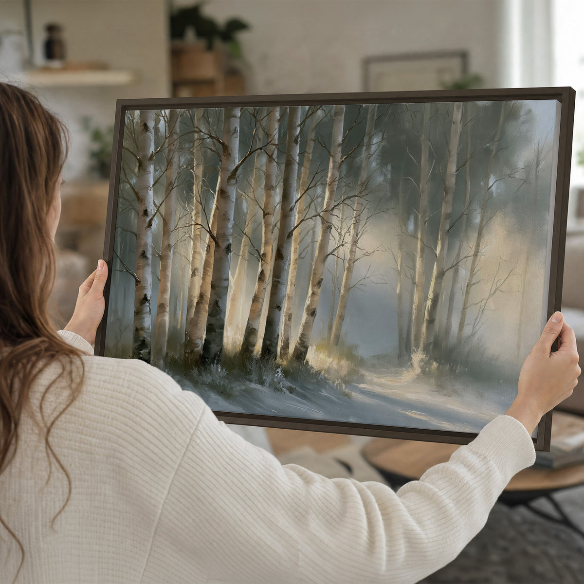 A softly lit woodland path winding between pale birch trunks single framed canvas wall art held in hands